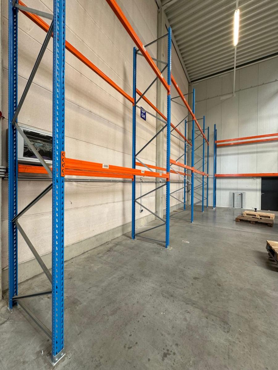 Palettenregal mit blauen Ständern und orangen Traversen entlang einer Hallenwand